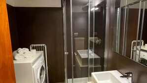 Une salle de bain moderne avec une douche à parois de verre, un lave-linge encastré et un grand miroir.