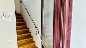Una escalera de madera con barandilla negra que lleva a una puerta con panel de vidrio.