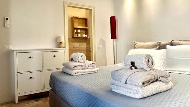 Habitación de hotel con cama, mesita de noche, armario y un pequeño estante con artículos de aseo.