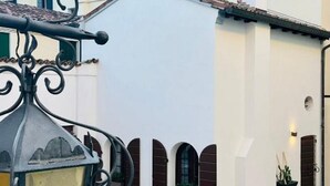 Un patio con un edificio blanco, contraventanas marrones y un farol de metal.