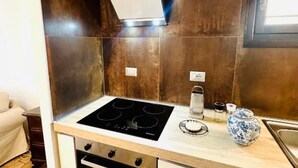 Una cocina compacta con tope de inducción negro, horno integrado y pileta de acero inoxidable.