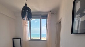Ein Schlafzimmer mit einem Bett, einem Fenster mit Blick auf den Strand, einem Spiegel und einer Deckenleuchte.