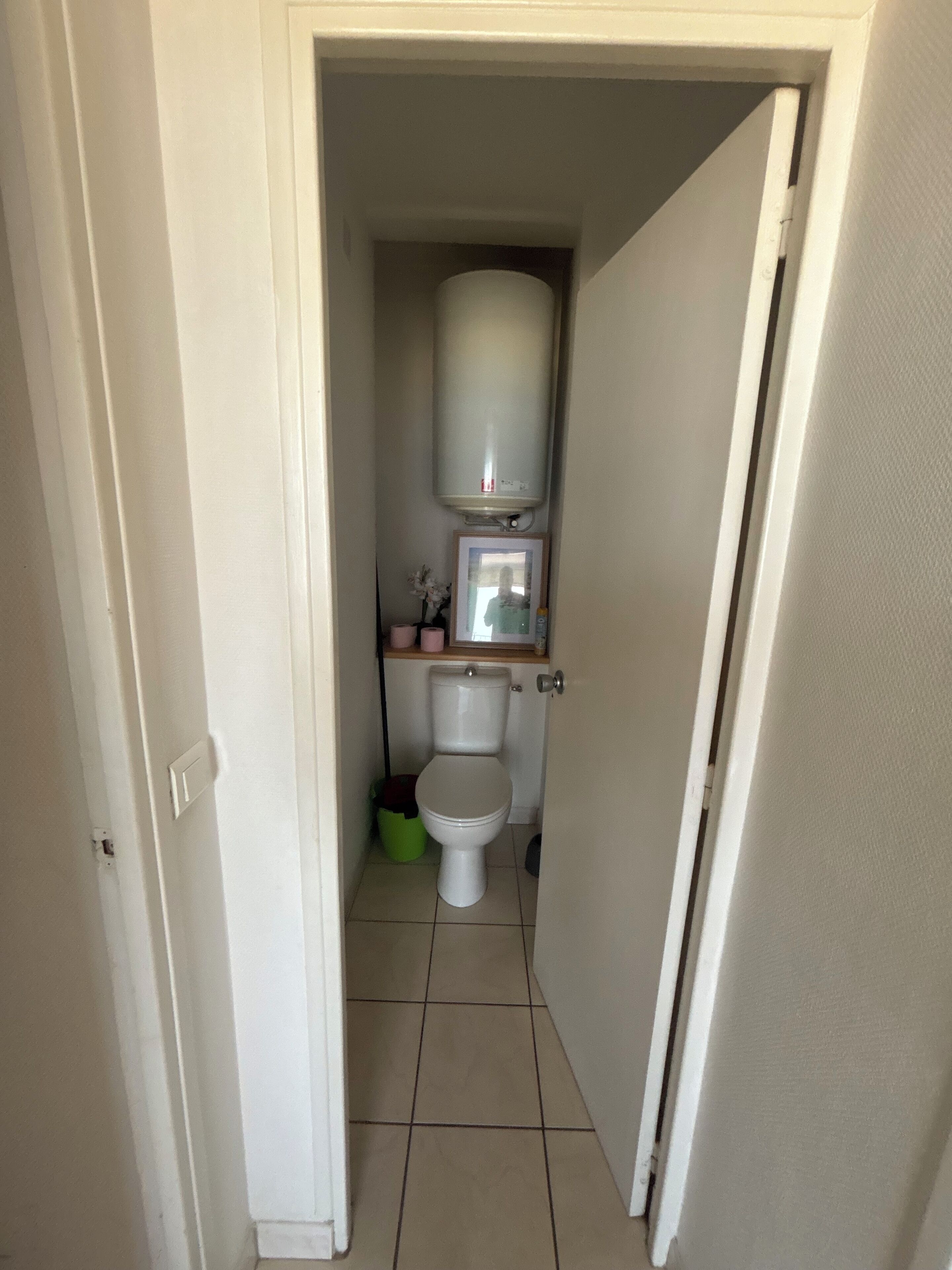 Een kleine, smalle badkamer met een toilet, een witte wastafel op een zuil en een spiegel boven de wastafel.