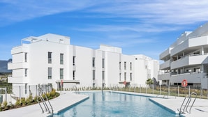 A modern building with a swimming pool, white exterior, and balconies.