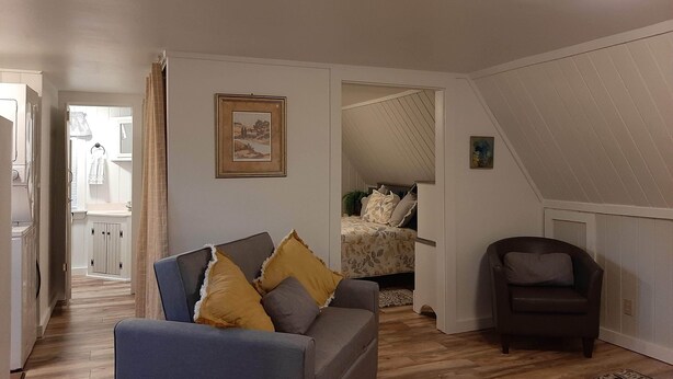 Una sala acogedora con un sofá, una silla y una cama al fondo.
