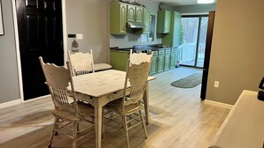 A dining area with a wooden table and chairs, a kitchen with green cabinets, and a view of the outdoors through a sliding glass door. - Retreat on Lake Milton 2 bed (Berlin Center)