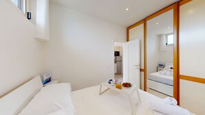 A hotel room with a bed, a small table with a tray of breakfast, a mirror, and a view of the kitchen. - Casa Marisol by Bookinggardalake (Manerba del Garda)