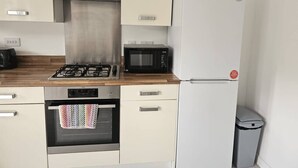 Cocina compacta con estufa a gas, microondas, horno y refrigerador blanco.