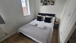 Un dormitorio con cama, ventana, mesita de noche y un cuadro en la pared.