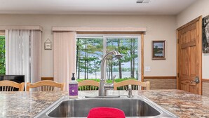 A kitchen with a granite countertop, stainless steel sink, and wooden chairs.