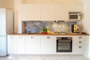 Une cuisine moderne avec des meubles blancs, un crédence à motifs bleus et blancs, un four à micro-ondes, une cuisinière à gaz et un four traditionnel.