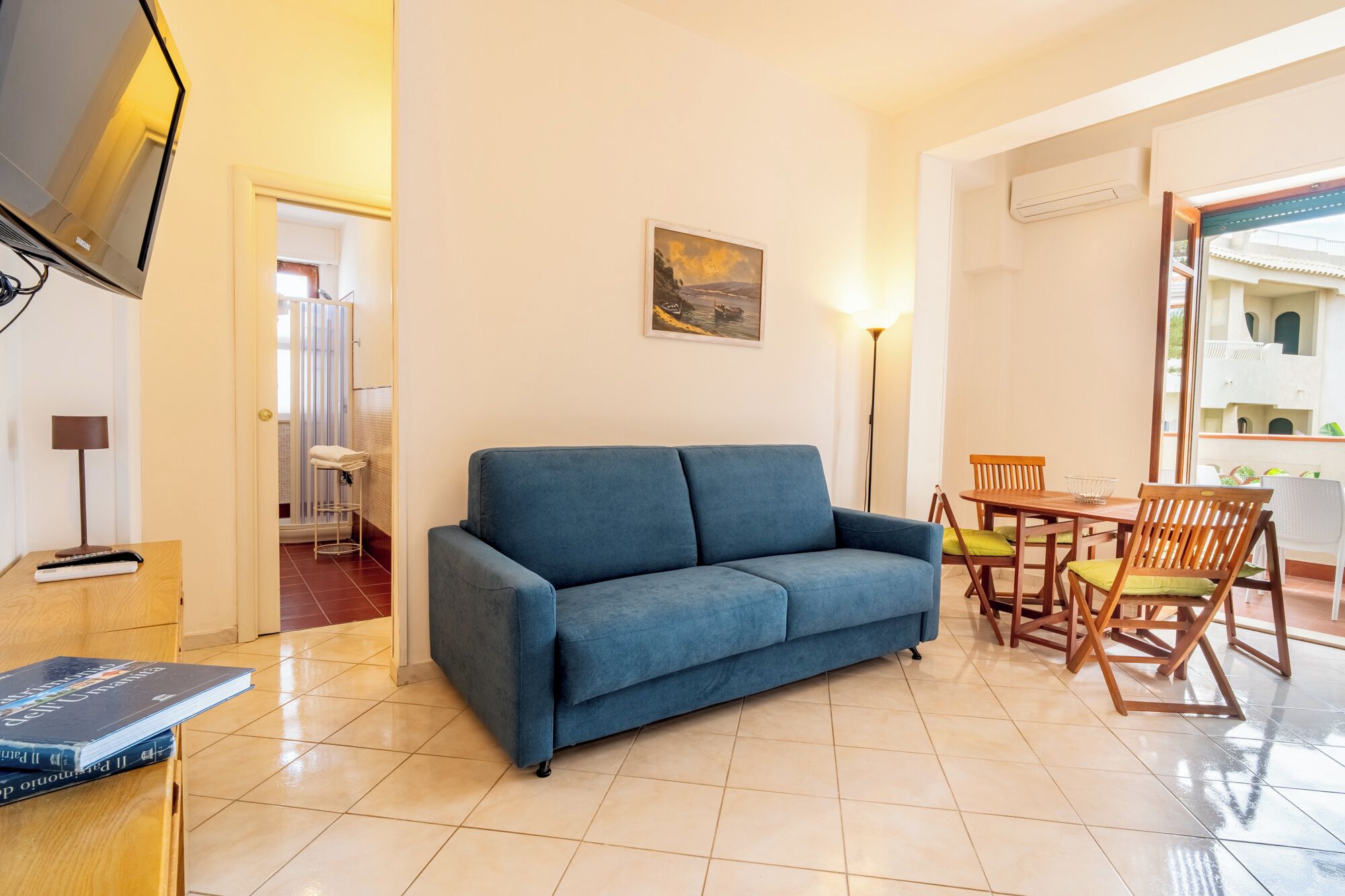 A living room with a sofa, a dining table with chairs, a TV, and a painting on the wall.