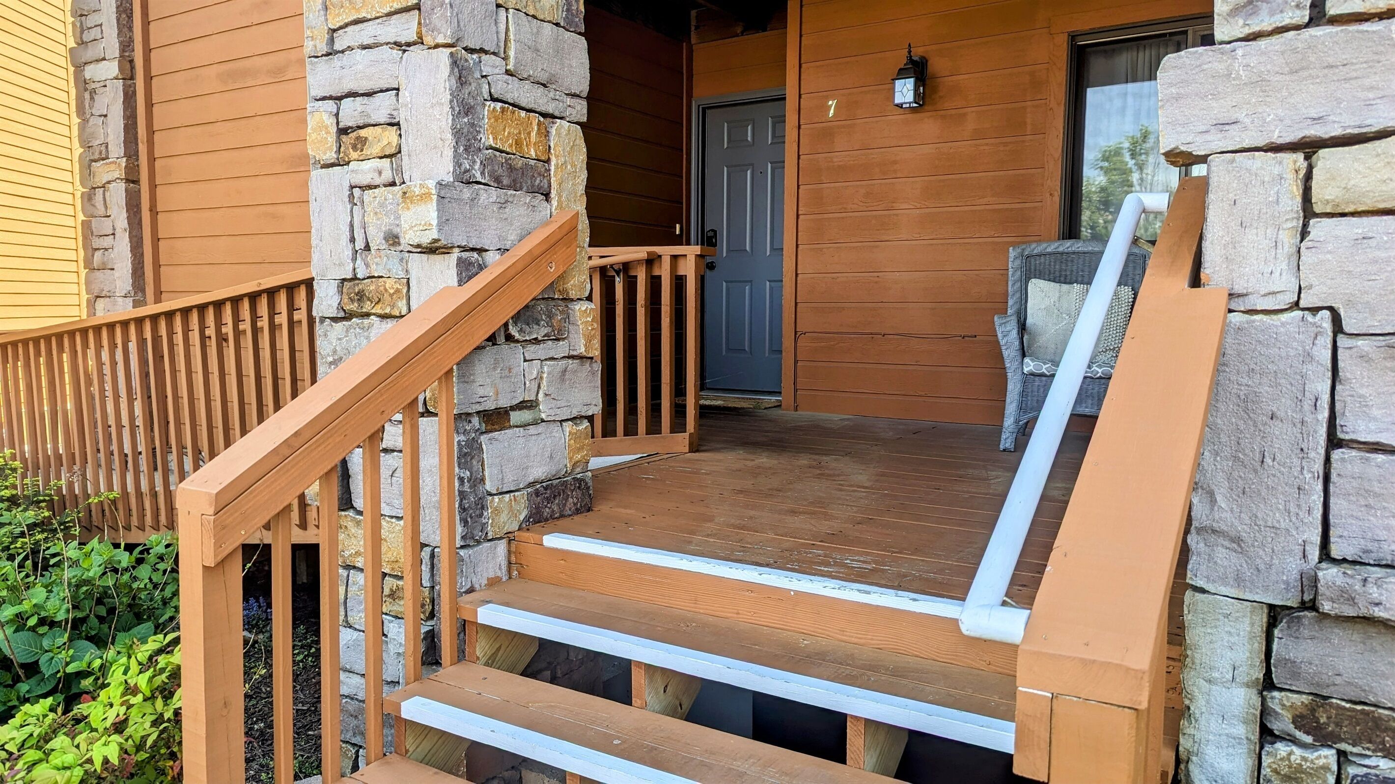 A wooden staircase leading to a stone-walled entrance, with a door and a lantern on the wall.