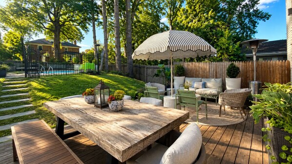 A wooden deck with a table and chairs, surrounded by a wooden fence and greenery.