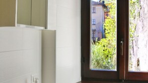 Un baño con ventana, dispensador de toallas y pared de azulejos blancos.