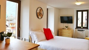 Una habitación de hotel con una cama, televisor, cómoda, planta y ventana.