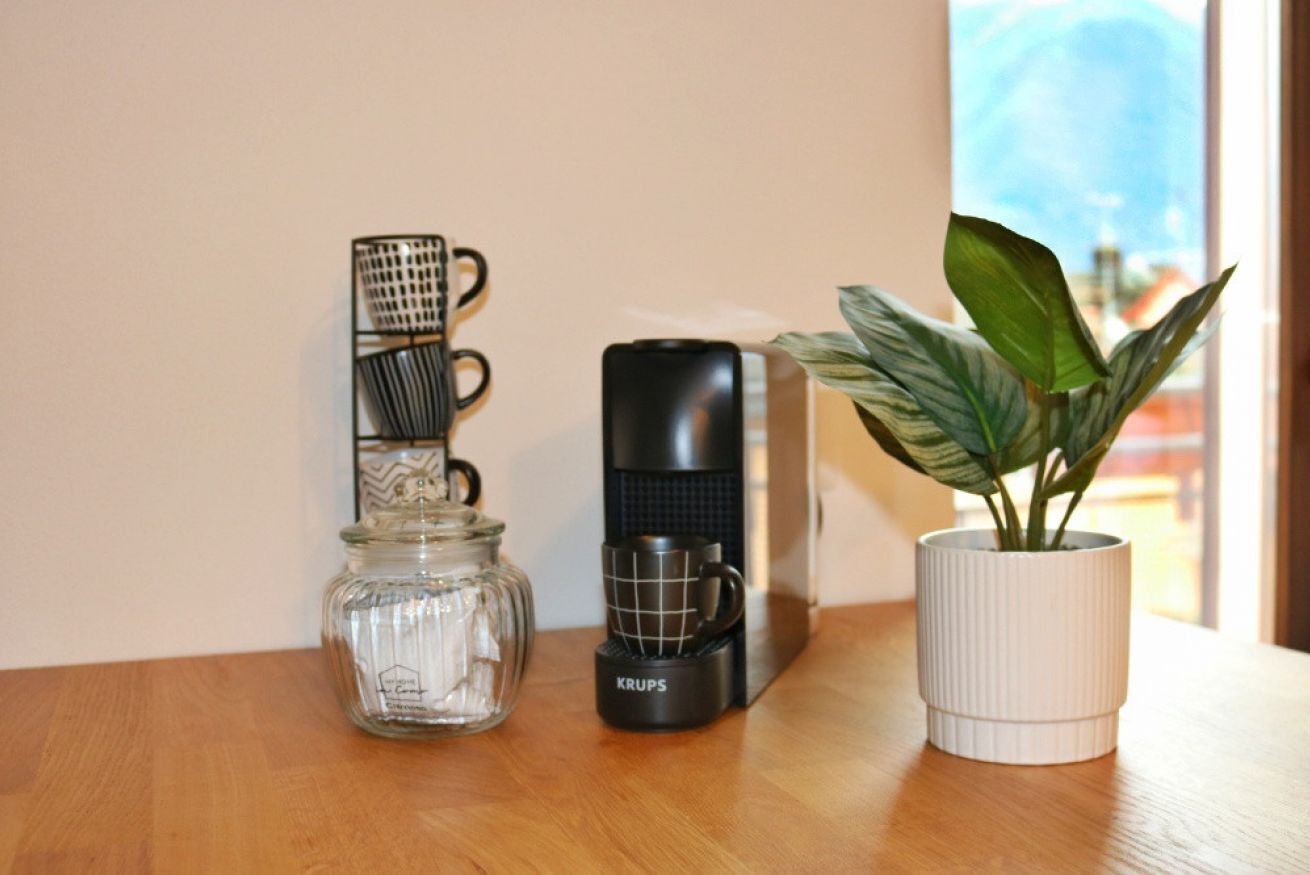 A coffee maker, a glass jar, and a potted plant on a wooden table.