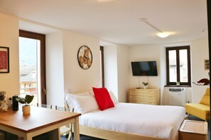 Een hotelkamer met een bed, een televisie, een houten dressoir, een bureau en een raam.