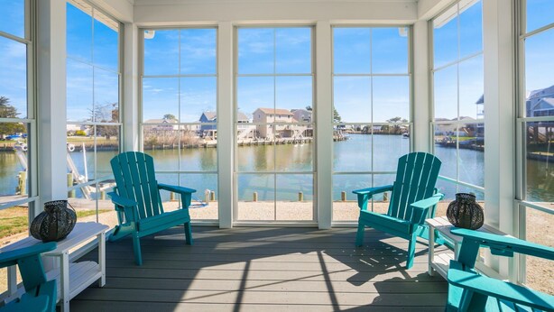 A covered outdoor area with two turquoise Adirondack chairs, a small table, and a decorative vase. - The Lighthouse | Luxury Waterfront Retreat w/ Dock, Fireplace, Pools, Marina, & Golf (Greenbackville)