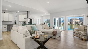 A spacious living area with a large sectional sofa, a coffee table, and a view of a marina through large sliding glass doors. - The Lighthouse | Luxury Waterfront Retreat w/ Dock, Fireplace, Pools, Marina, & Golf (Greenbackville)