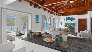 A modern kitchen with granite countertops, a dining area with a sofa, and a large TV. - Magens Bay - dining - POOL - Incredible views (St. Thomas)