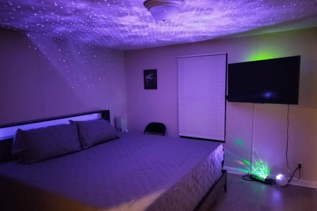 Un dormitorio con cama, televisor montado en la pared y proyector de techo.