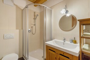 A bathroom with a glass-enclosed shower, a white sink, a mirror, and wooden cabinets.