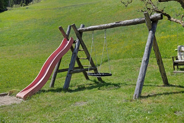 Une balançoire en bois avec un toboggan, installée dans un champ d’herbe.