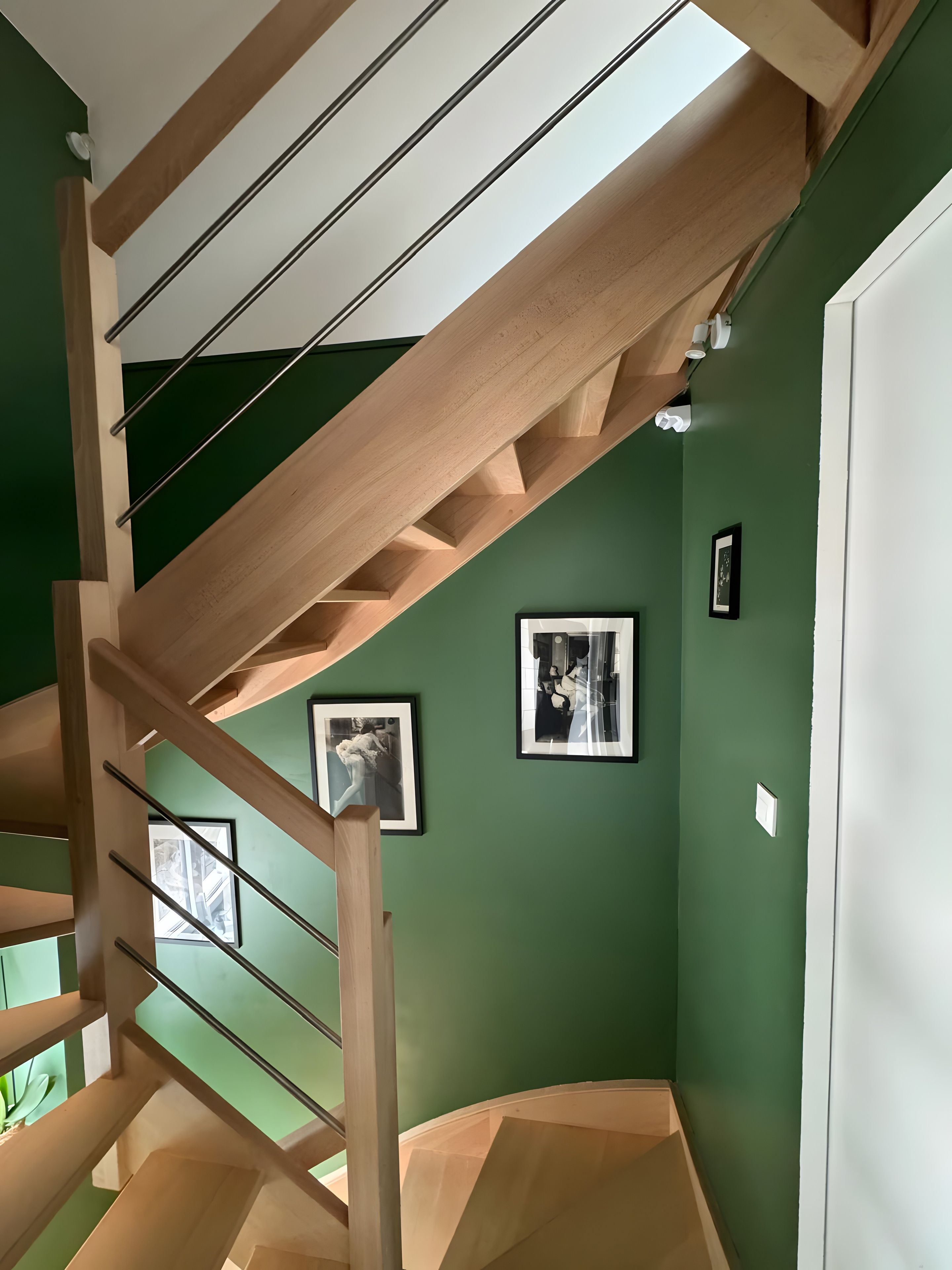 A wooden staircase with a green wall and framed pictures.