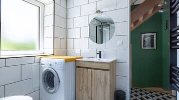 Une petite salle de bain équipée d’un lave-linge, d’un lavabo, d’un miroir et de toilettes.