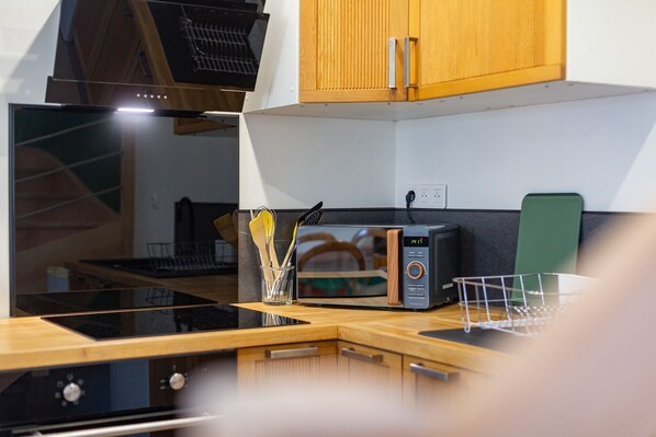 Una cocina con microondas, un recipiente de vidrio con utensilios y armarios de madera.