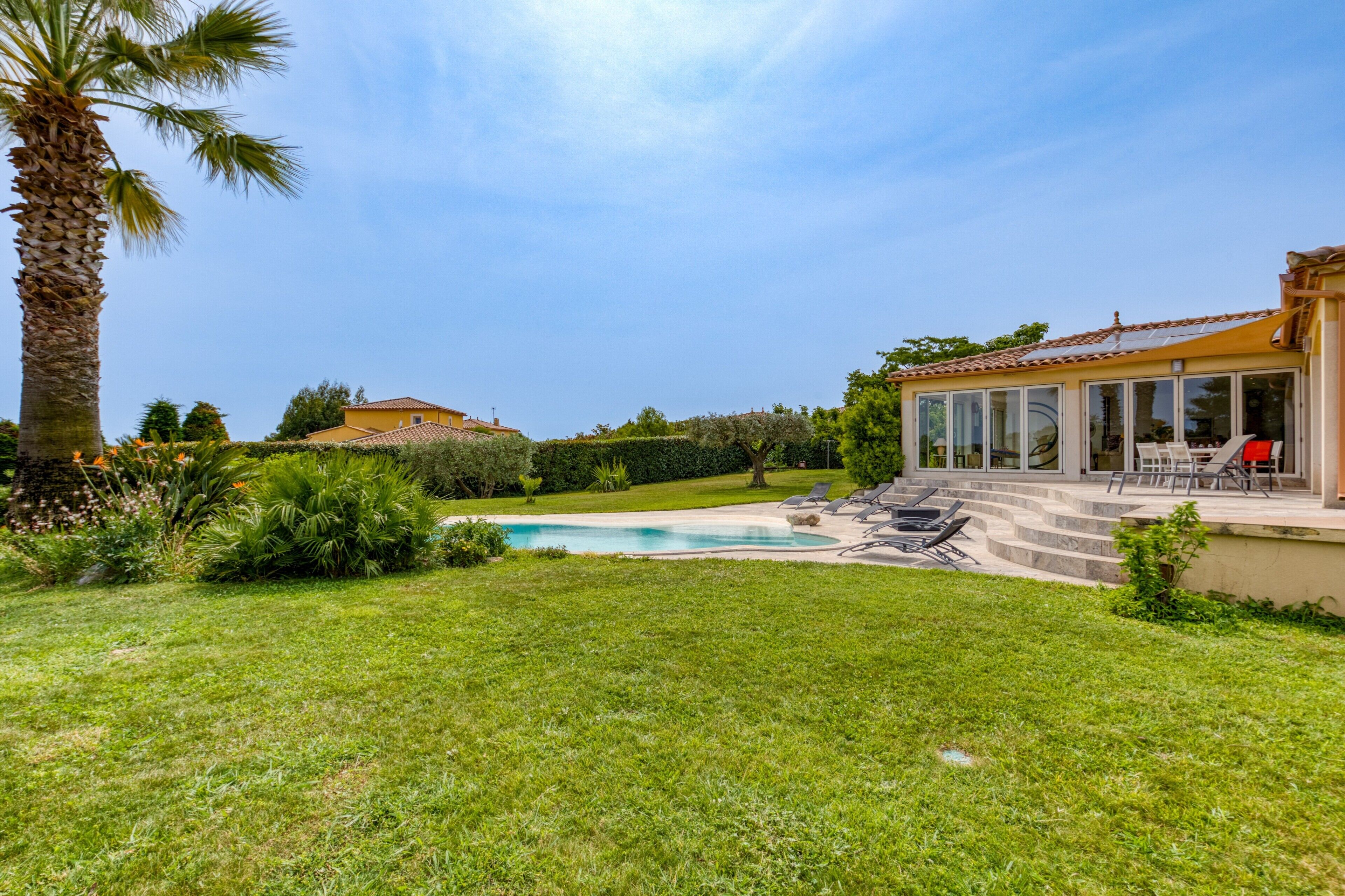 Ein Wohnhaus mit Schwimmbad, Terrasse und Gartenmöbeln sowie einem gepflegten Rasen.