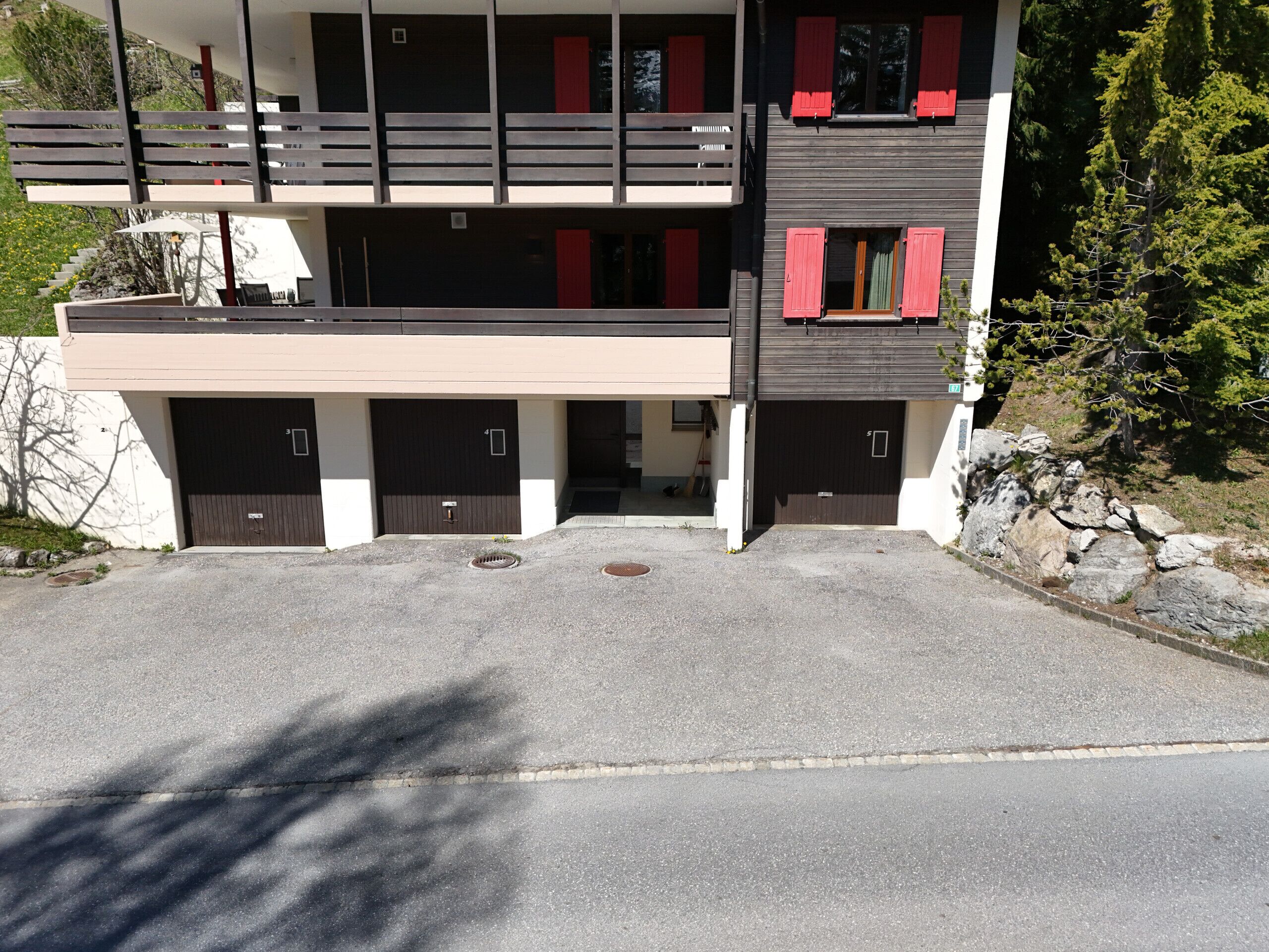 A two-story building with a garage entrance, a balcony, and red shutters on the windows.