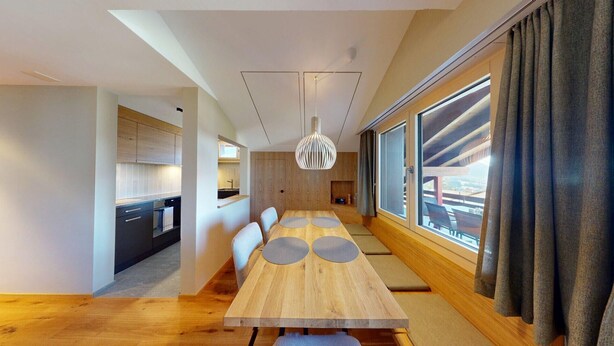Un comedor moderno con una mesa y sillas de madera, una lámpara colgante y vistas amplias a través de grandes ventanales.