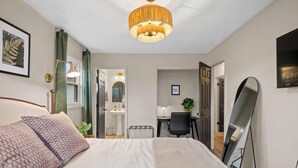 Habitación de hotel con una cama grande, un escritorio con una silla, un espejo y una lámpara colgante.