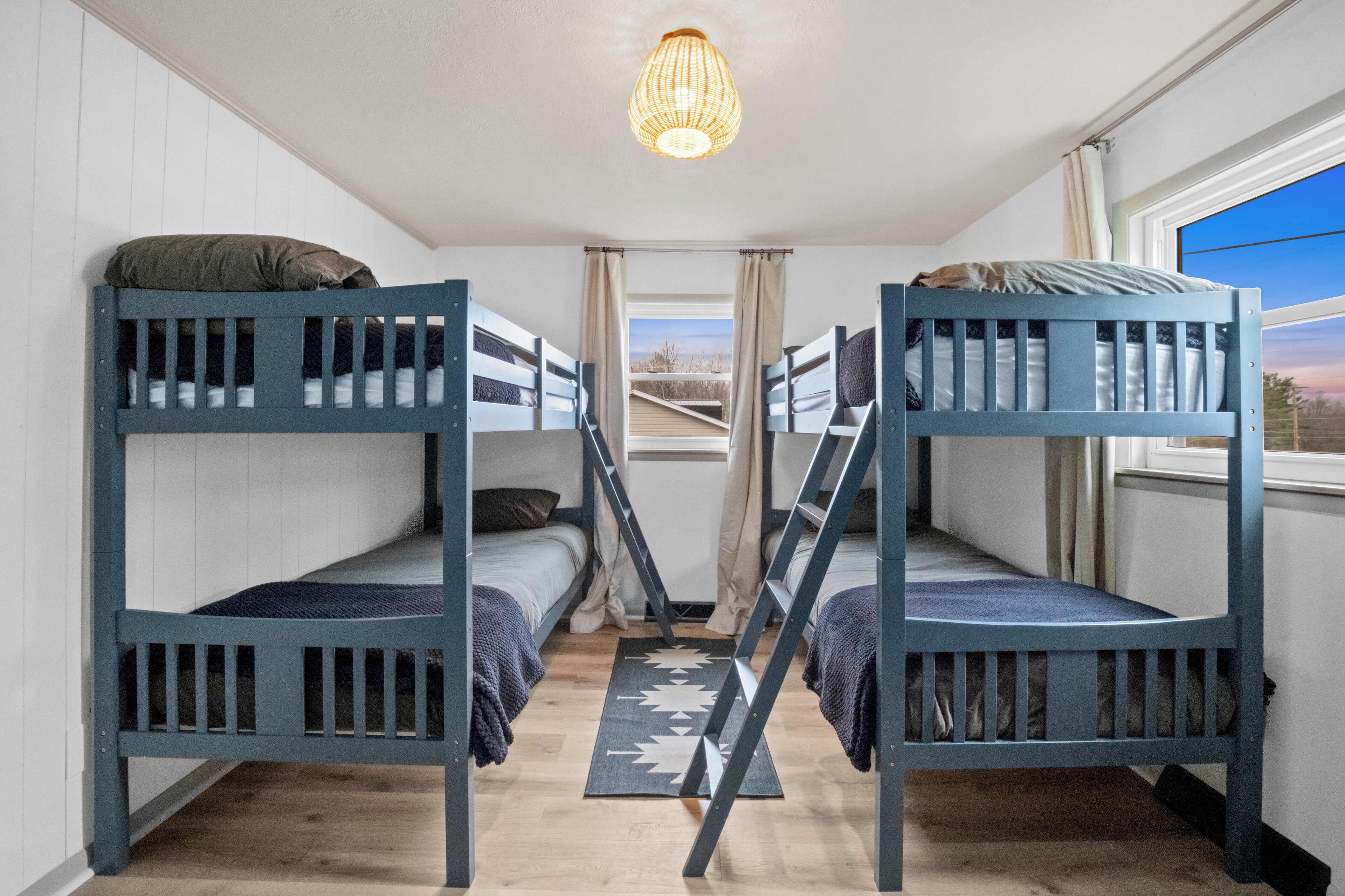 A room with two bunk beds, a wooden floor, a ceiling light, and a view through a window.