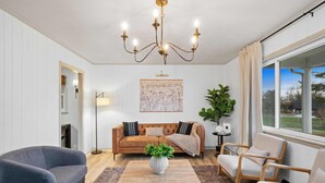 Una sala de estar con un sofá marrón, dos sillones, una mesa de centro y una araña.