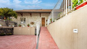 A stone building with a wooden door, a brick pathway, and a white railing with potted plants.