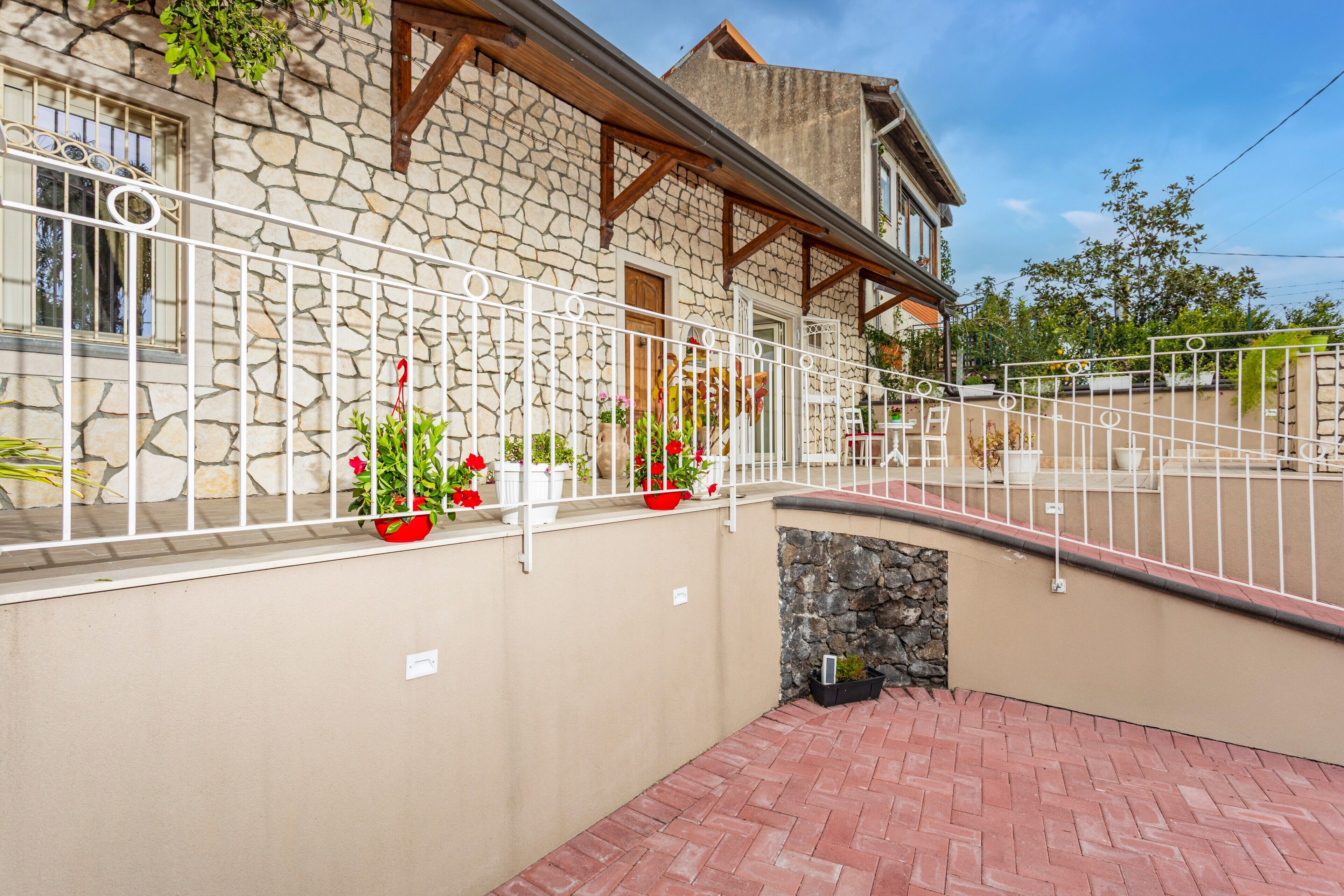 A stone building with a balcony, potted plants, and a brick pathway.