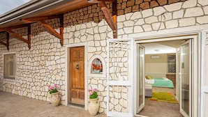A stone building with a wooden door, a white gate, and a room with a bed and a green rug.