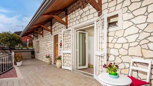 A stone building with a patio, a white chair, and a table with a flower vase.