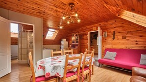 A wooden interior with a dining table, chairs, a sofa, and a kitchen area. - Holiday Home 'Des Granges' with Mountain Views, Private Terrace & Wi-Fi (Tréminis)