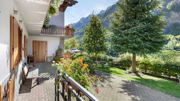 Una cabaña con balcón, contraventanas de madera y un jardín con flores y árboles.