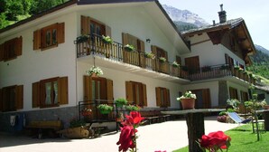 Un edificio de dos pisos con contraventanas de madera, balcones con macetas de flores y una chimenea de piedra.