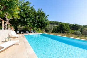 Una piscina con sillas de descanso, rodeada de árboles y con vistas a un paisaje montañoso.