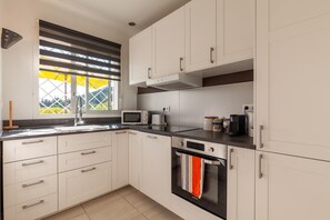 A modern kitchen with white cabinets, a microwave, a kettle, and a window with blinds. - Apartment 'La Naronne' with Shared Pool, Private Terrace and Wi-Fi (Bandol)