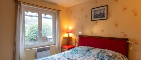 A bedroom with a bed, a window with curtains, a bedside lamp, and a framed picture on the wall.