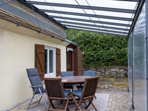 A covered patio with a table and chairs, a wooden door, and a stone wall.