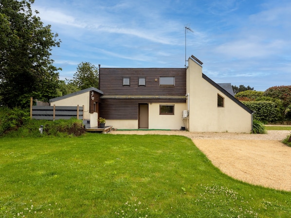 A two-story house with a sloped roof, a front porch, and a small garden area.