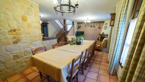 Un espace repas comprenant une longue table, des chaises, un lustre, des murs en pierre et un escalier.
